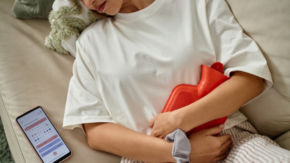 Woman experiencing painful menstrual cramps while tracking periods on mobile app, highlighting fertility and reproductive health concerns